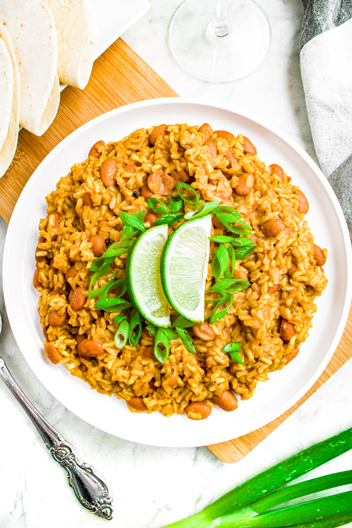 Overhead photo of a round white plate loaded with pinto beans and rice topped with lime wedges and sliced green onions