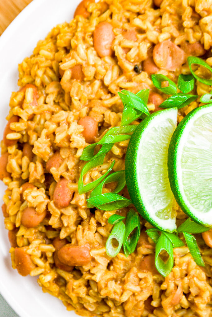 Overhead close up photo of half a plate of pinto beans and brown rice garnished with sliced scallions and lime wedges