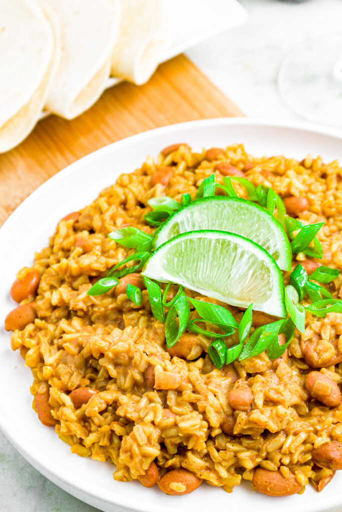 Overhead photo of a plate of rice and pinto beans on a wood board topped with lime wedges and green onions.