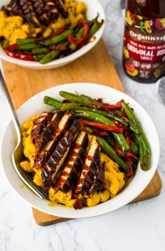 Overhead photo of a bowl on a long wooden plank with bbq tofu, sweet potato mac and cheese, and vegan green beans