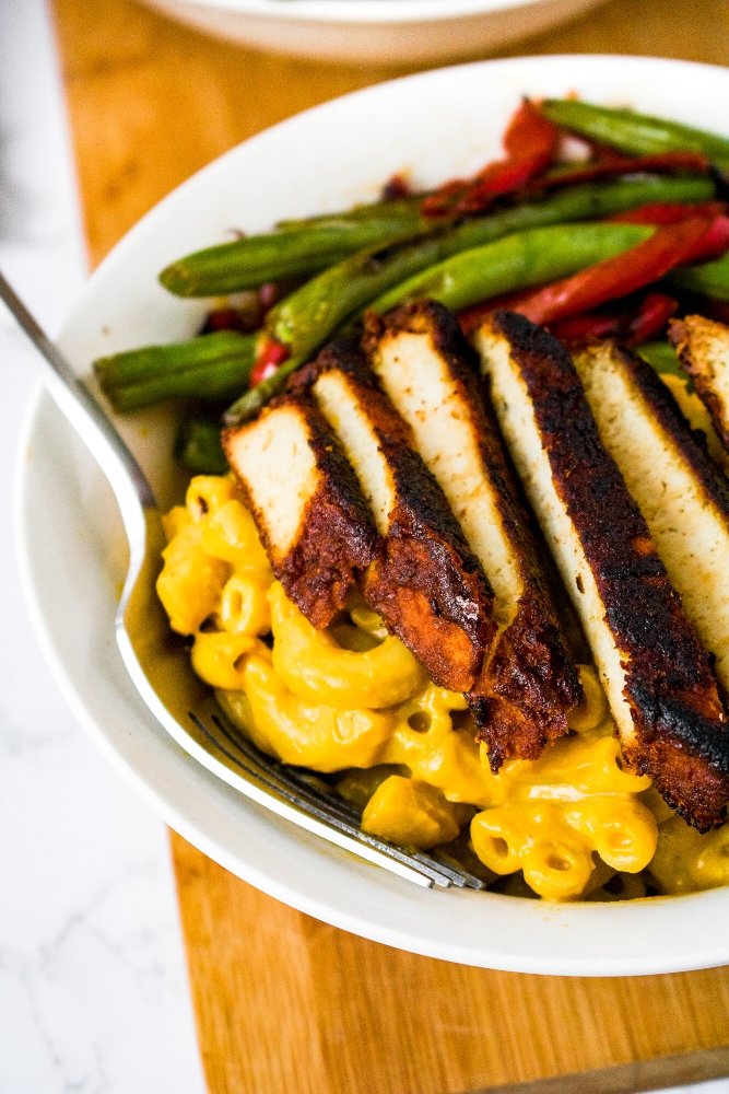 Overhead close up photo of a round white bowl with mac and cheese, sliced bbq tofu, and seared green beans