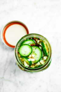 Overhead photo of quick and easy whiskey pickles in an open mason jar with the lid next to it