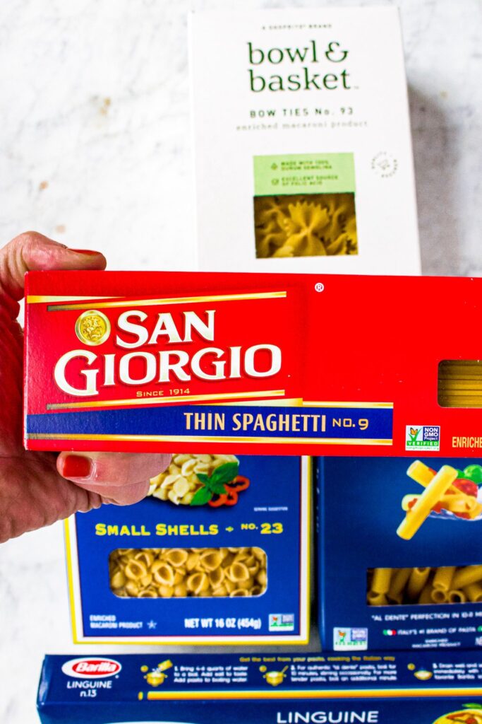 Overhead photo of a hand holding a red rectangular box of San Giorgio thin spaghetti pasta