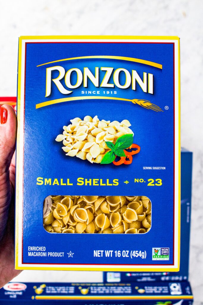 Overhead photo of a hand holding a box of Ronzoni small shell pasta