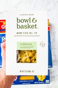 Overhead photo of a hand holding up a box of Bowl and Basket bowtie pasta