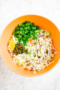 Overhead photo of a bowl filled with coleslaw mix, scallions, lemon zest, and capers