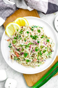 Overhead photo of a round white plate piled high with lemon tahini slaw and lemon wedges in the upper left corner