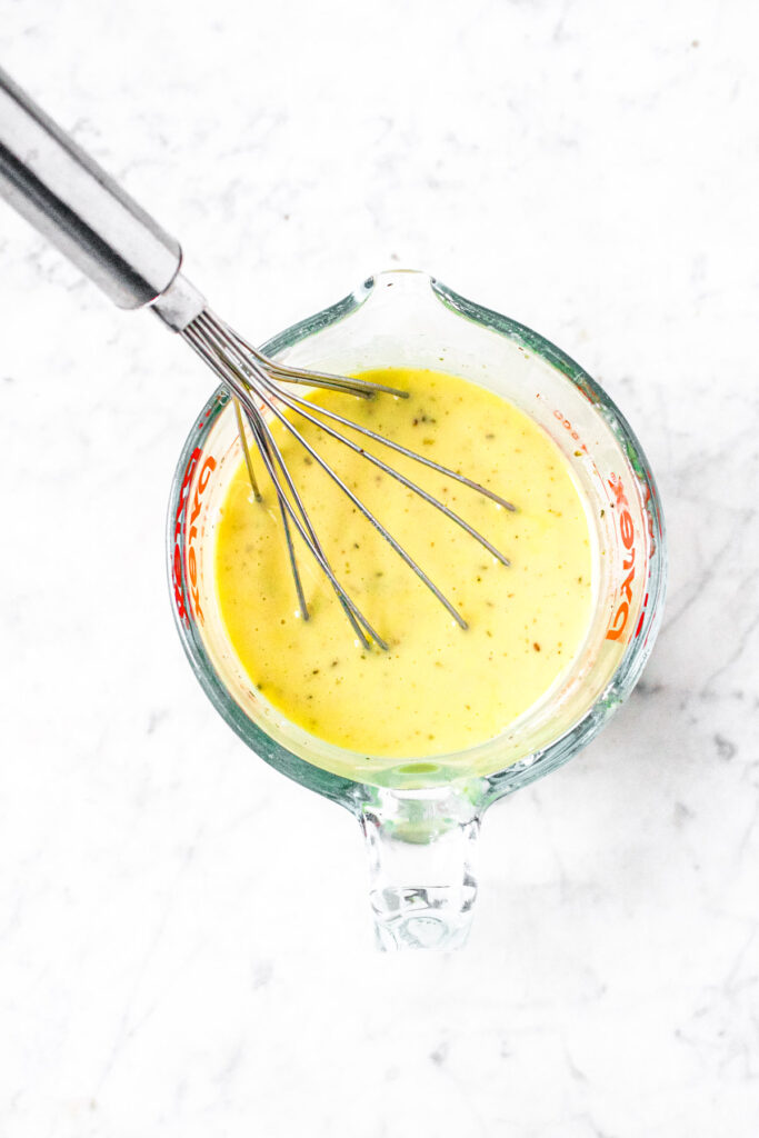 Overhead photo of a glass measuring cup with creamy vegan Italian dressing and a metal whisk sticking into it