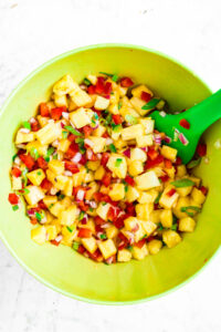 Overhead photo of a mixing bowl with pineapple pico de gallo in it and a silicone spatula digging into it