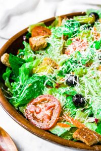 Overhead close up photo of a large green Italian salad in a bamboo bowl
