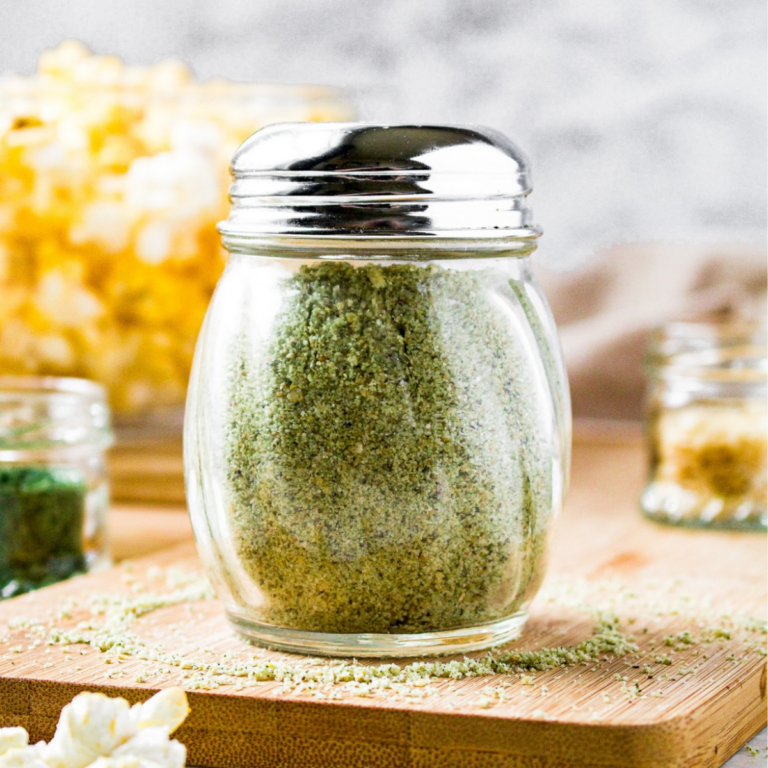 A head-on view of vegan ranch powder in a classic restaurant shaker jar with a metal lid. There is a bowl of popcorn behind the jar.