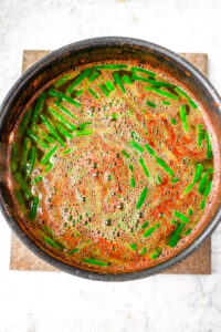 Overhead photo of green beans cooking in a tomato broth in a large pot