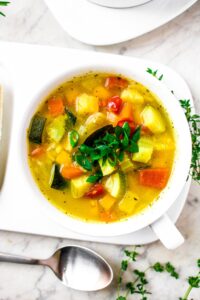 Overhead image of a bowl of vegetable soup with squash and zucchini and barley but no tomatoes