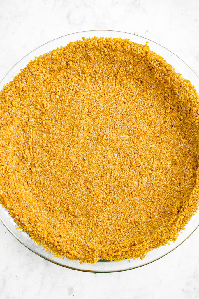 Overhead close up photo of a graham cracker pie crust in a glass pie dish
