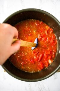 Overhead photo of a hand stirring a large soup pot full of diced tomatoes