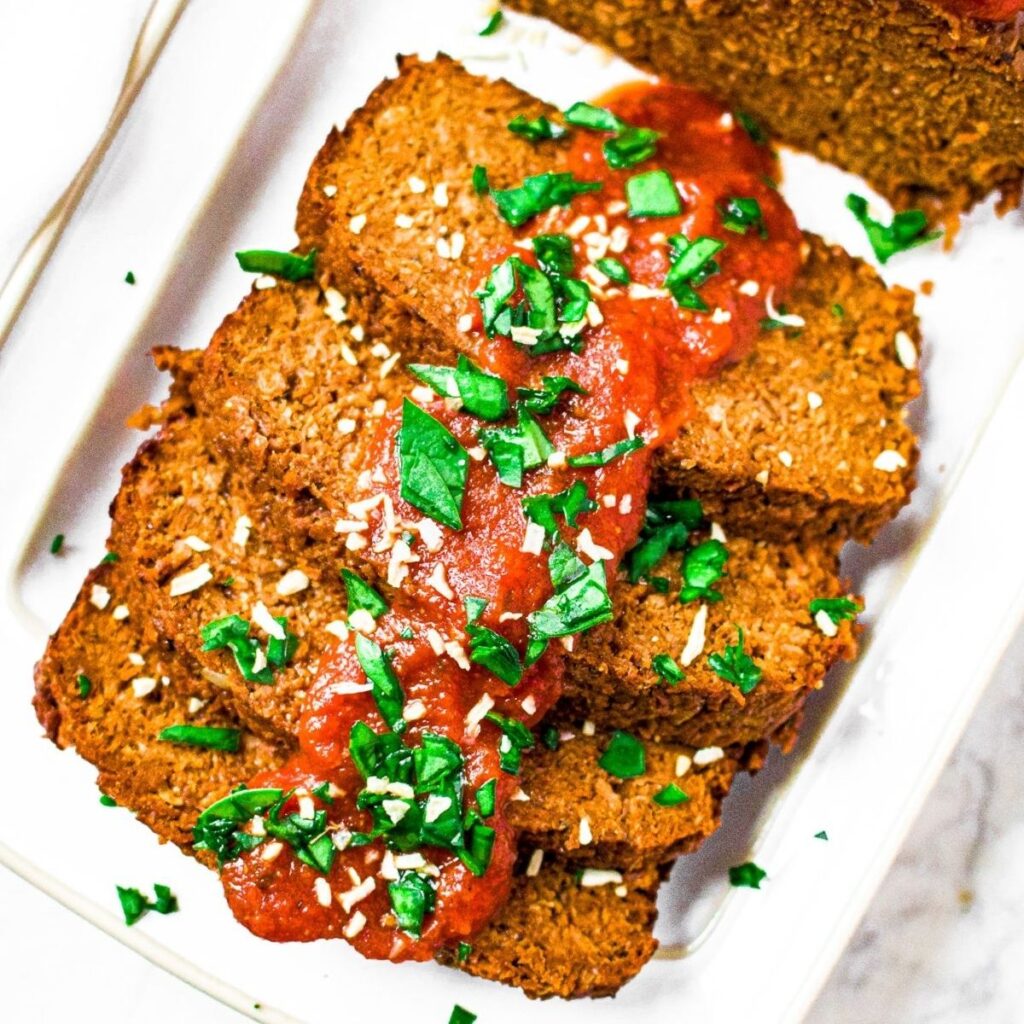 Overhead photo of a partially sliced vegan meat loaf on a white rectangular plate