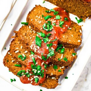 Overhead photo of a partially sliced vegan meat loaf on a white rectangular plate