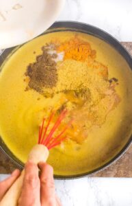 Overhead photo of a hand with a whisk stirring a pot of pumpkin soup with coconut milk