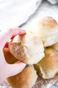 Overhead photo of a hand pulling a bread roll from a pile of them
