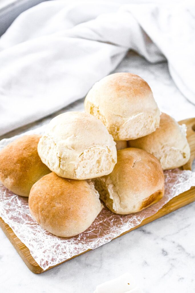 Close up head-on photo of a pile of bread rolls on a rectangular cutting board