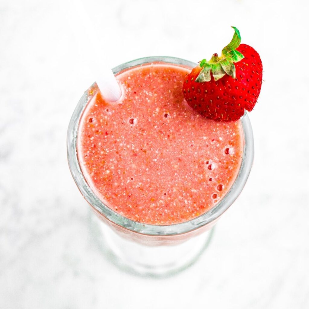 Overhead photo of a cherry Frozen Garden smoothie in a glass with a straw and strawberry on the rim