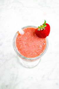 Overhead photo of a cherry smoothie in a glass with a straw and strawberry on the rim