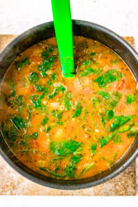 Overhead photo of a large soup pot of Italian Vegetable Soup being stirred by a lime green silicone spatula