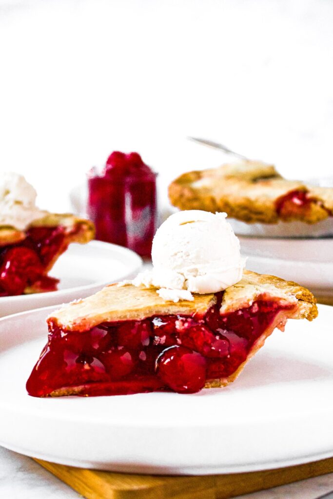 A head-on photo of a slice of cherry pie topped with a scoop of vanilla ice cream