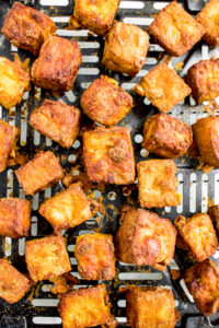 Overhead close up photo of air fryer tofu cubes cooking in the basket