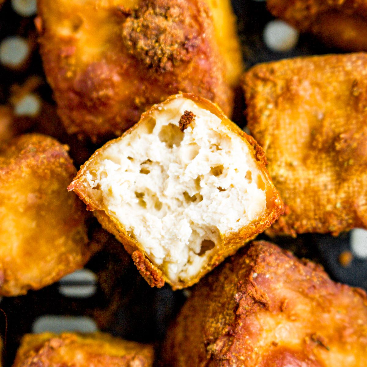 Overhead close up photo of a pile of crispy tofu cubes. The top one has a bite taken out of it.