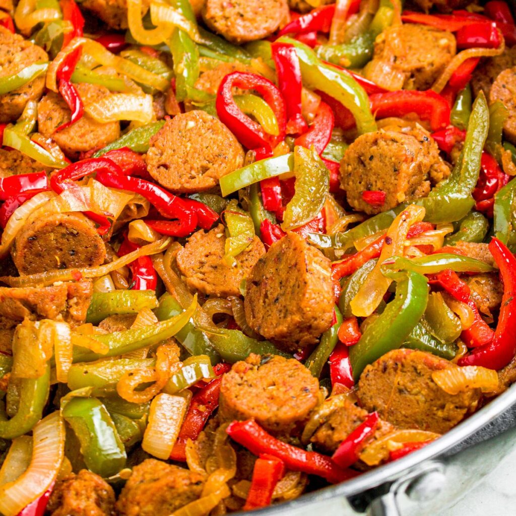 Overhead zoomed in photo of a sliced vegan sausages cooked with onions and bell peppers in a large skillet