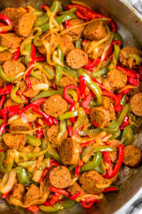 Overhead close up photo of sliced vegan sausage and peppers in a large metal pan