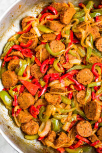 Overhead photo of sliced vegetarian sausage and peppers with onions in a large saute pan