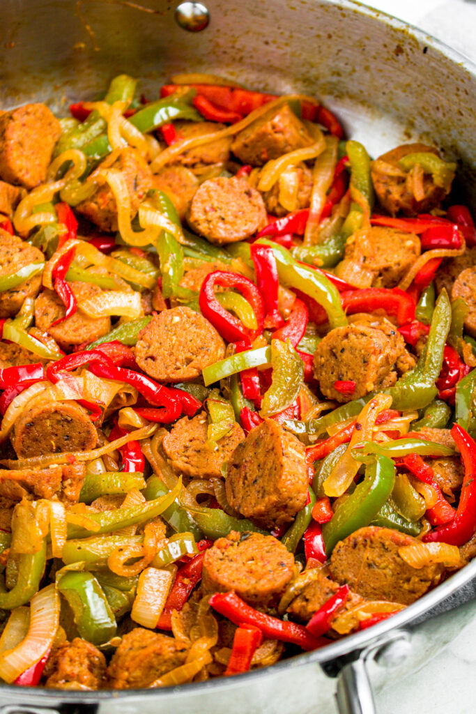 Overhead zoomed in photo of a sliced seitan sausage cooked with peppers and onions in a large skillet