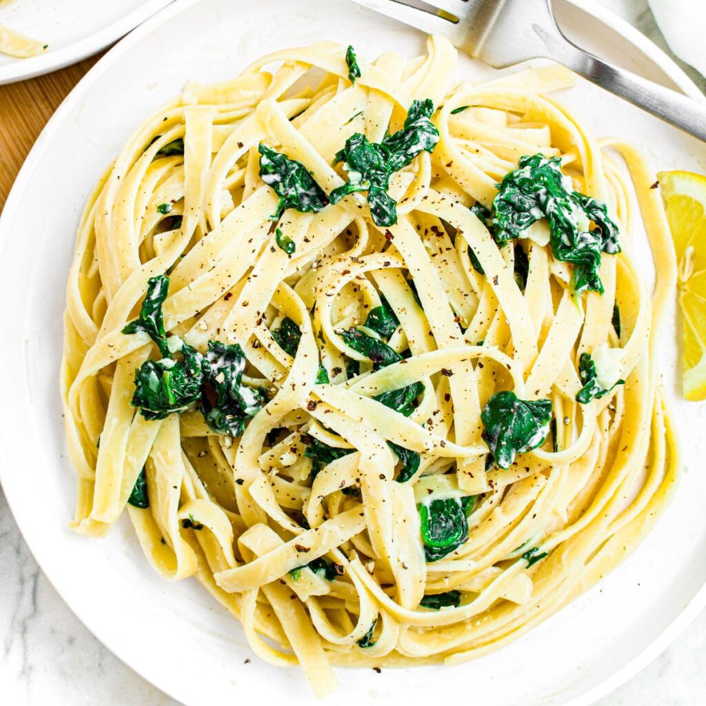 Close up overhead photo of a plate of creamy pasta with spinach and lemon wedges