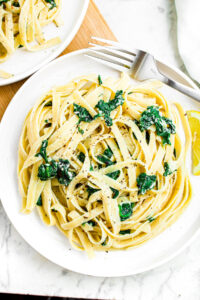Overhead photo of a round white plate of creamy spinach and fettuccine with a fork to the right side.