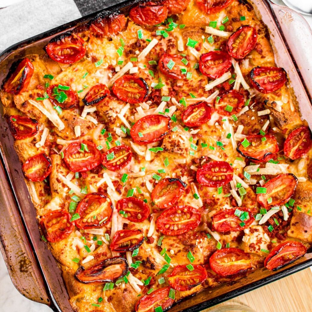 Close up overhead photo of a square casserole dish with vegan breakfast strata topped with halved grape tomatoes and green herbs