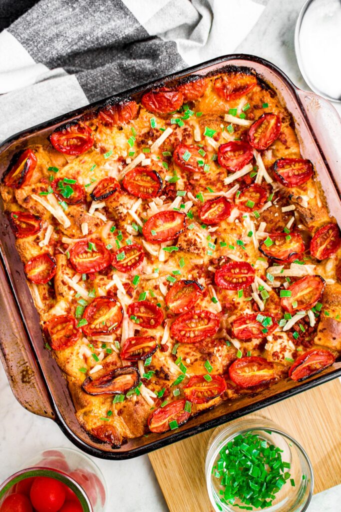 Overhead photo of a square baking dish with vegan breakfast strata topped with halved grape tomatoes and green herbs