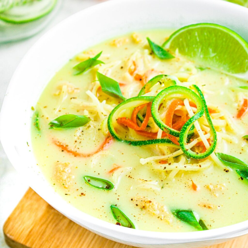 Zoomed in photo of a bowl of zucchini ramen soup garnished with a lime wedge in a creamy coconut curry broth