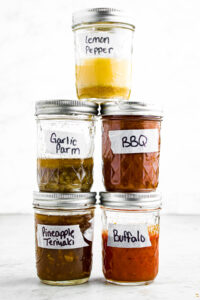 Head on photo of a tower of 5 vegan wing sauces: lemon pepper, garlic parm, bbq, pineapple teriyaki, and buffalo