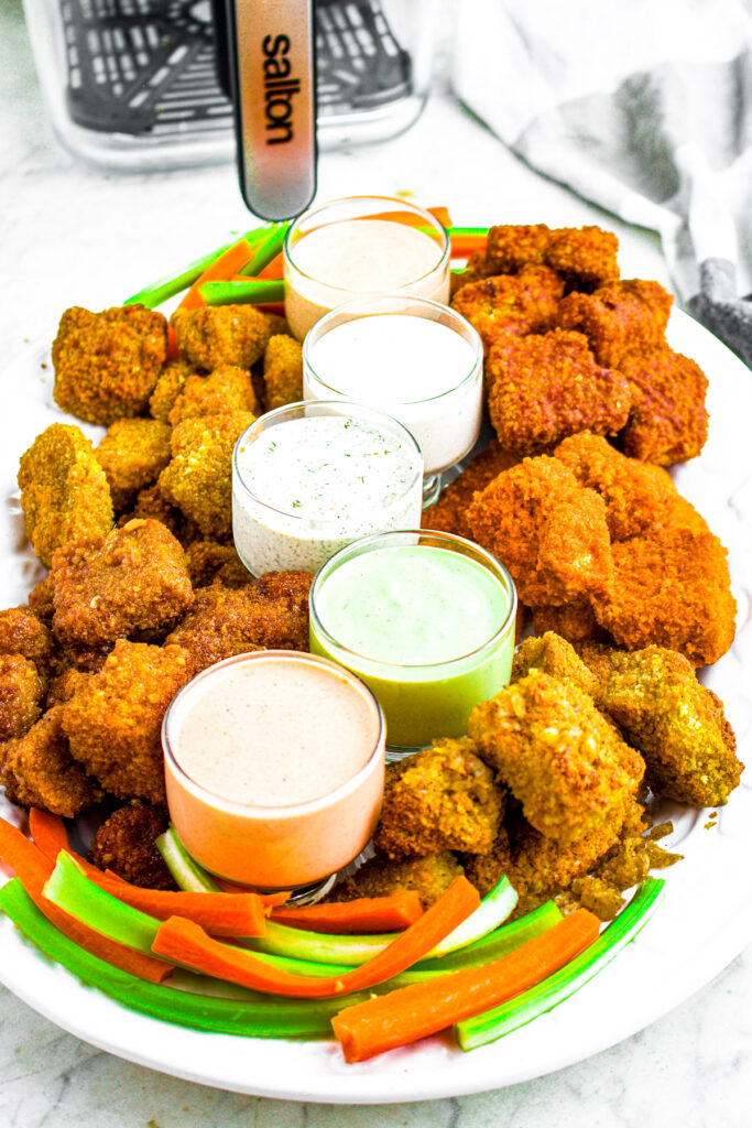 Head on close up photo of a large plate of vegan chicken wings and vegan ranch sauces in front of a Salton flip and cook basket in the background