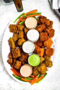 Overhead photo of a large oval white plate filled with various flavors of air fryer tofu wings and dairy-free ranch dips