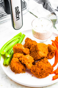 Overhead photo of a pile of vegan buffalo wings on a plate with celery, carrot sticks, and dip