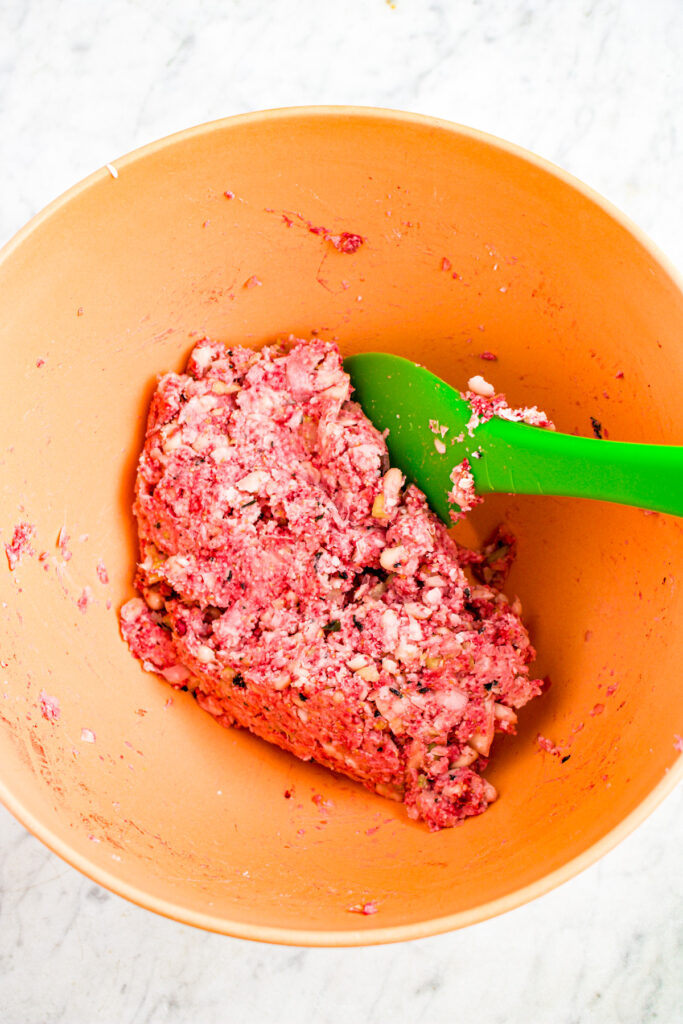 Overhead view of a large orange mixing bowl filled with a pink white bean mash being stirred with a lime green rubber spatula
