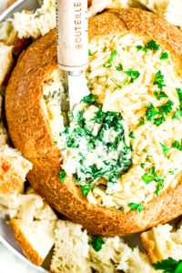 Close up view of a spoon digging into a vegan spinach artichoke dip in a bread bowl