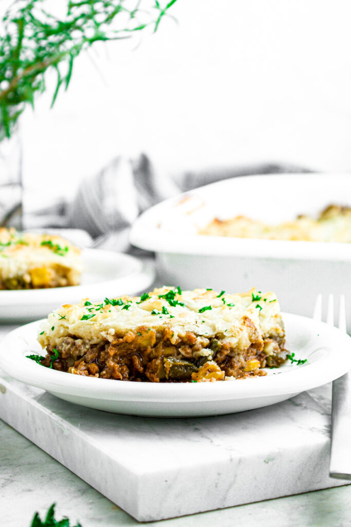 Head on view of a slice of vegetarian shepherd's pie on a round white plate topped with green herbs