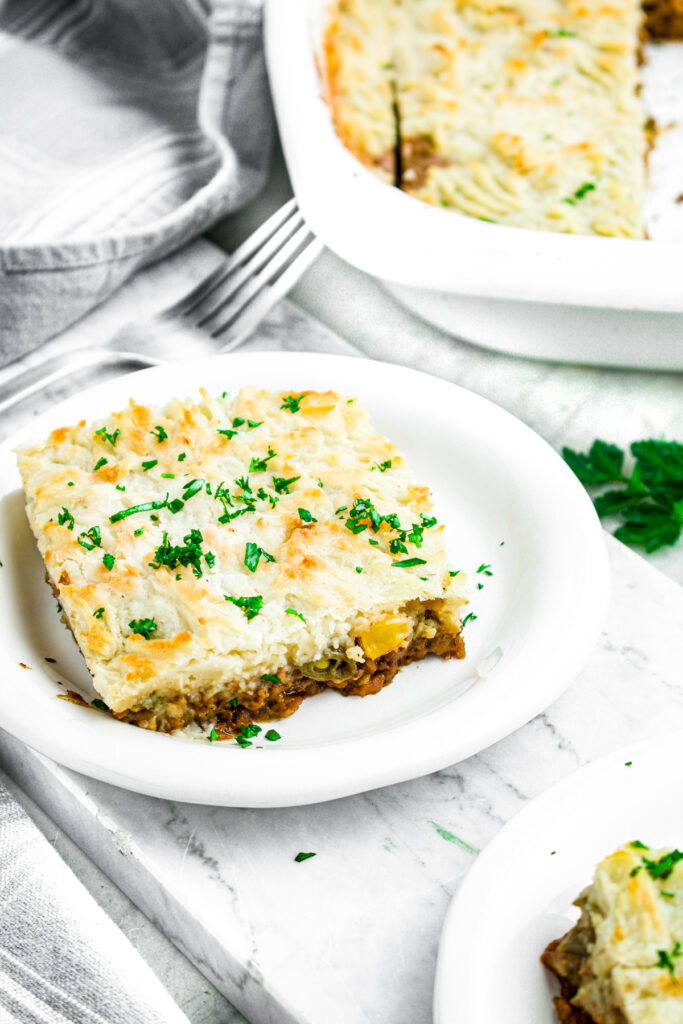 Overhead view of a slice of vegan shepherd's pie on a round white plate topped with green herbs