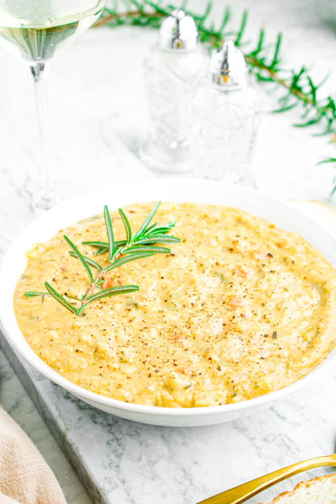 Overhead view of a round white bowl filled with creamy vegetable lentil soup with a sprig of rosemary sticking out of it on the left side