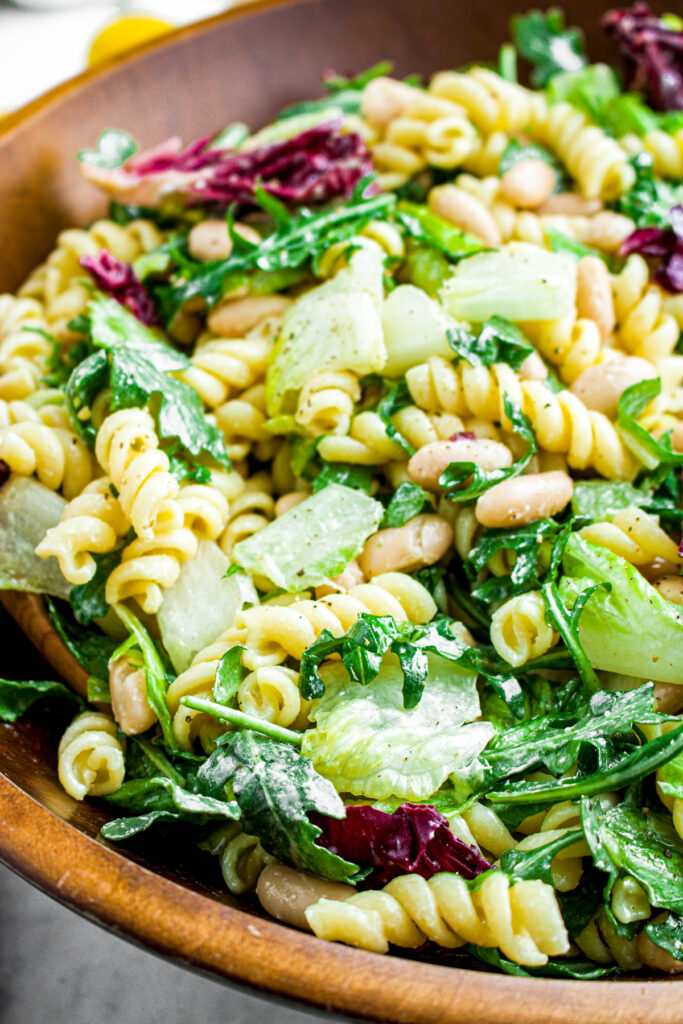 Overhead view of a round bamboo bowl full of lemon arugula pasta salad