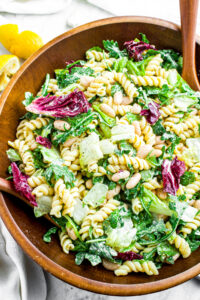 Overhead view of a round dark wood bamboo bowl full of creamy vegan lemon pasta salad
